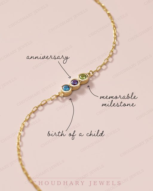 A yellow gold chain bracelet with three bezel-set gemstones, blue, purple and green, with handwritten labels reading anniversary, memorable milestone and birth of a child.