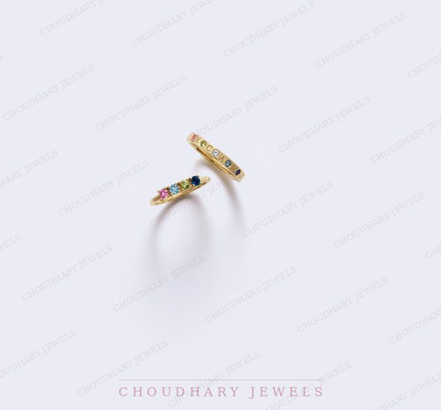 Two yellow gold stacking rings set with rows of small colored gemstones, on a pale lavender background.