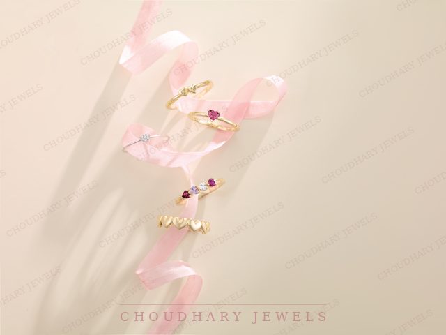 Three yellow gold rings with colored gemstones, one with the word mom, arranged on a pink ribbon.