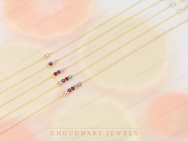 Several fine yellow gold chain bracelets, each with a short row of small colored gemstones, over a soft pastel background.