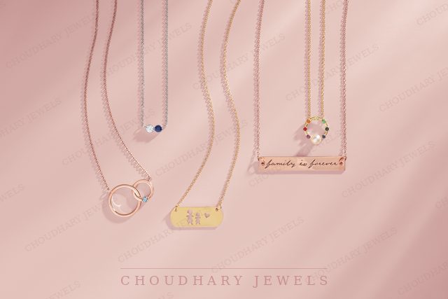 Rose, yellow and white gold necklaces with small gemstones, including interlocking circles, a heart and engraved bar pendants, on a pink background.