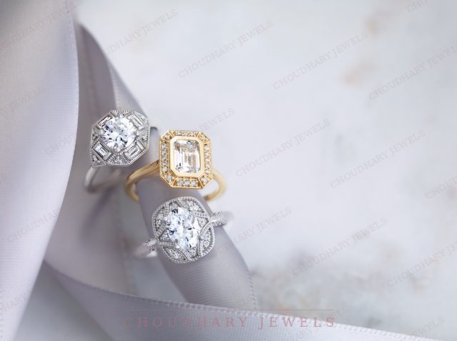 Three vintage-style engagement rings on a lavender ribbon: a white gold hexagon halo, a yellow gold emerald-cut halo and a white gold round halo with milgrain detail.