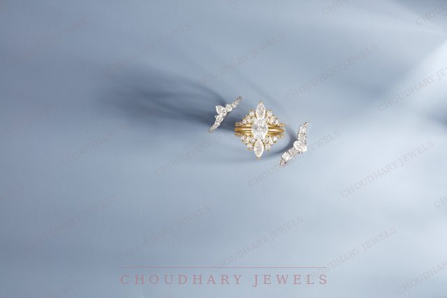A yellow gold marquise diamond engagement ring between two curved diamond bands, on a pale blue fabric background.