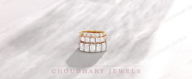 A stack of rose, yellow and white gold diamond bands set with emerald-cut diamonds, on white marble.