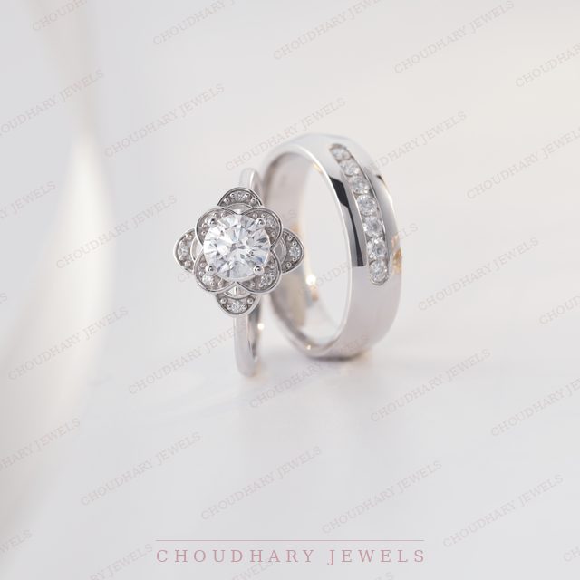 A white gold round diamond halo engagement ring with a petal-shaped halo, beside a white metal band with channel-set diamonds.
