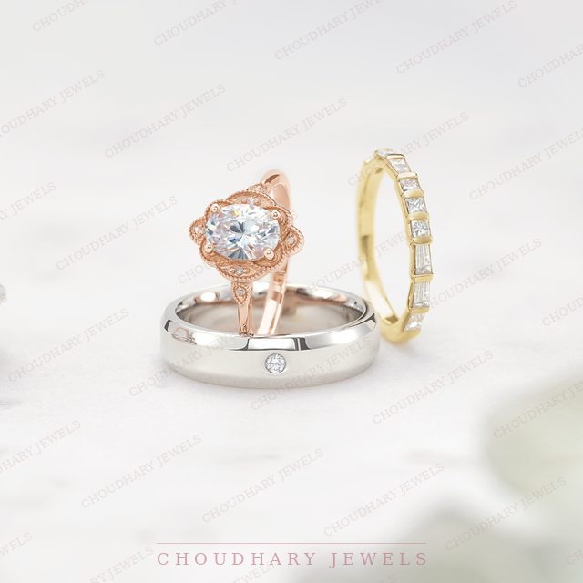 A rose gold oval diamond engagement ring with a petal halo, resting on a white metal band, beside a yellow gold baguette diamond band.
