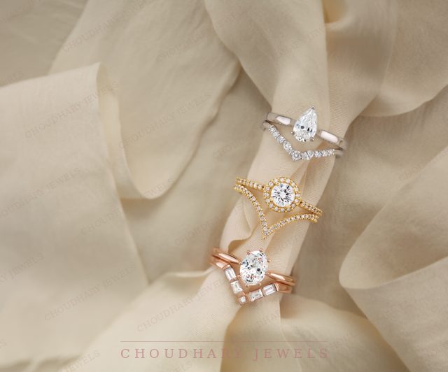 Three engagement rings with matching curved bands on cream silk: a white gold pear diamond, a yellow gold round diamond and a rose gold round diamond.