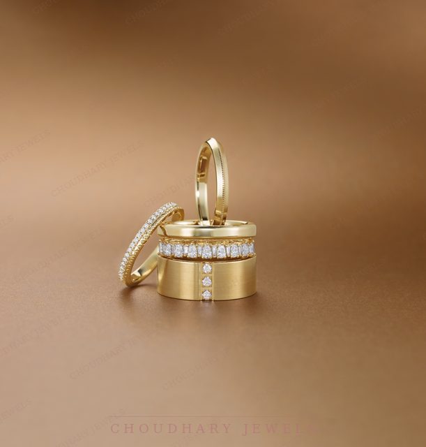 Stacked yellow gold bands, including a wide band set with a row of diamonds and vertical diamond accents, on a warm brown background.