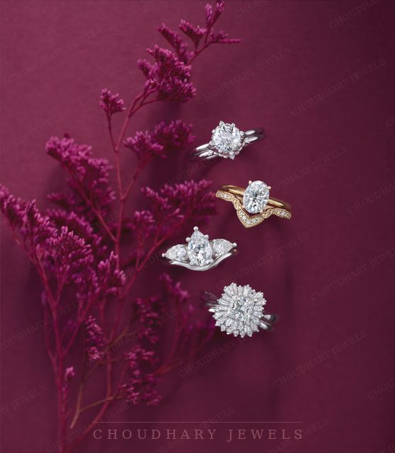 Four white and yellow gold diamond engagement rings, including halo, three-stone and curved-band styles, beside purple flowers on a purple background.
