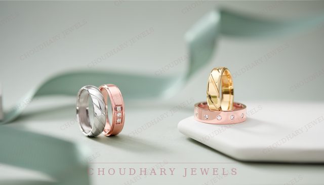 Two pairs of wedding bands: a white gold and a rose gold band, and a yellow gold band on a rose gold band with a pattern, beside a green ribbon.
