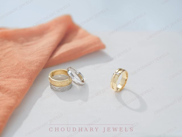 Two-tone wedding bands in yellow and white gold, with textured and patterned finishes, beside a coral linen cloth.