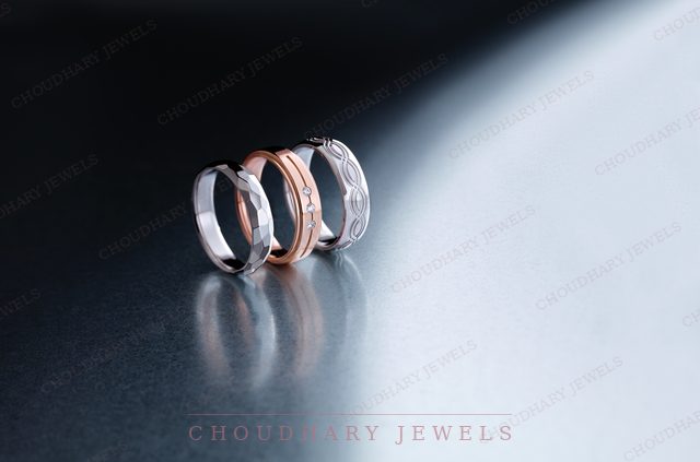 Three textured wedding bands in white, rose and white gold, standing on a dark reflective surface.