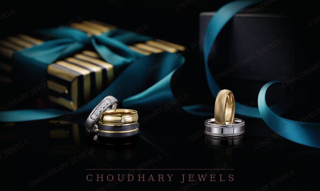 Men's wedding bands in white, yellow and blue-inlaid finishes, beside a gift box with a teal ribbon on a dark background.