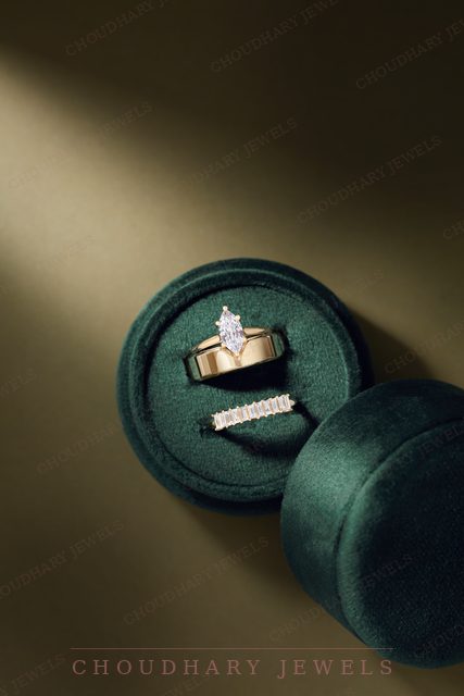 A yellow gold marquise diamond engagement ring and a diamond band in a green velvet ring box.