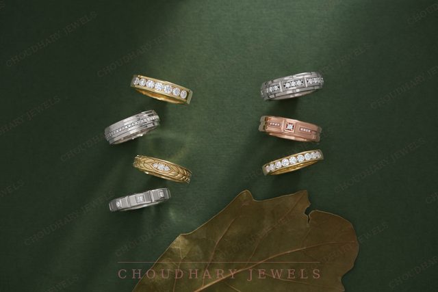 Six diamond wedding bands in yellow, white and rose gold, arranged in two rows on green fabric with a leaf.