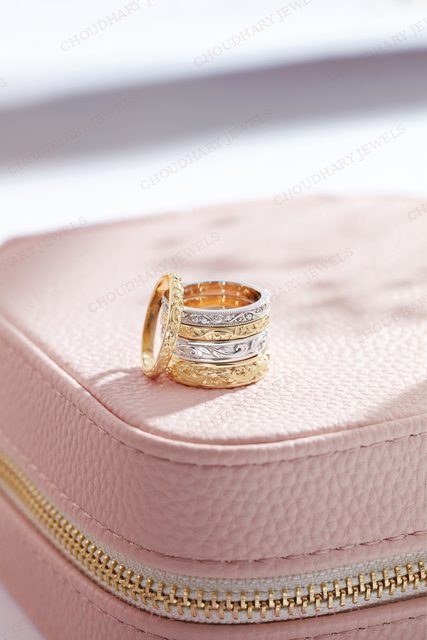 A stack of yellow, white and rose gold bands with engraved and diamond-set designs, on a pink leather jewelry case.