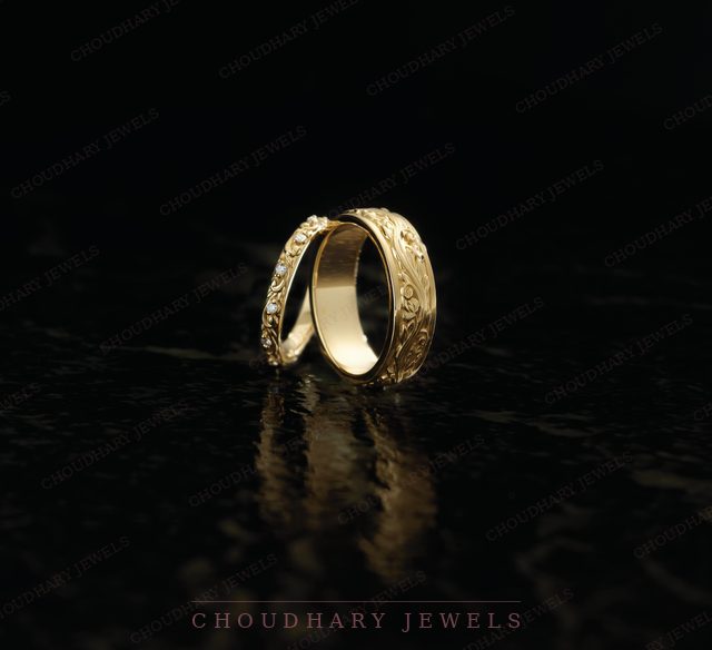 Two engraved yellow gold bands with small diamonds, on a black reflective surface.