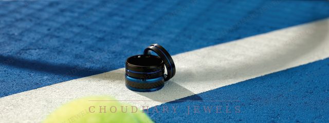 Two black men's bands with a blue stripe, on a blue tennis court beside a tennis ball.