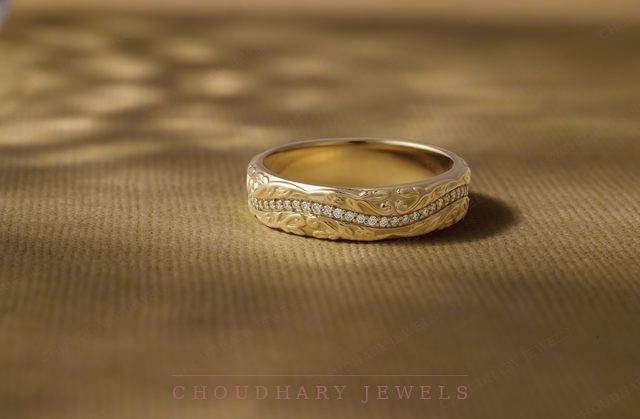 A yellow gold band with a wavy engraved pattern and a row of small diamonds, on gold fabric.