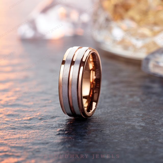 A rose and gray men's band with a grooved design, on dark stone.
